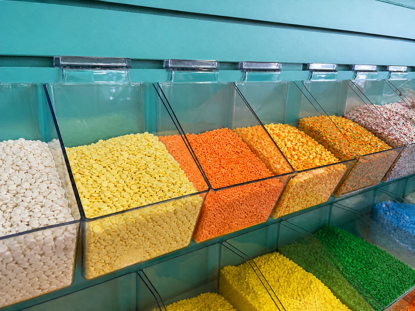 Close-up of cream, yellow, and orange slime sprinkle toppings in clear bins